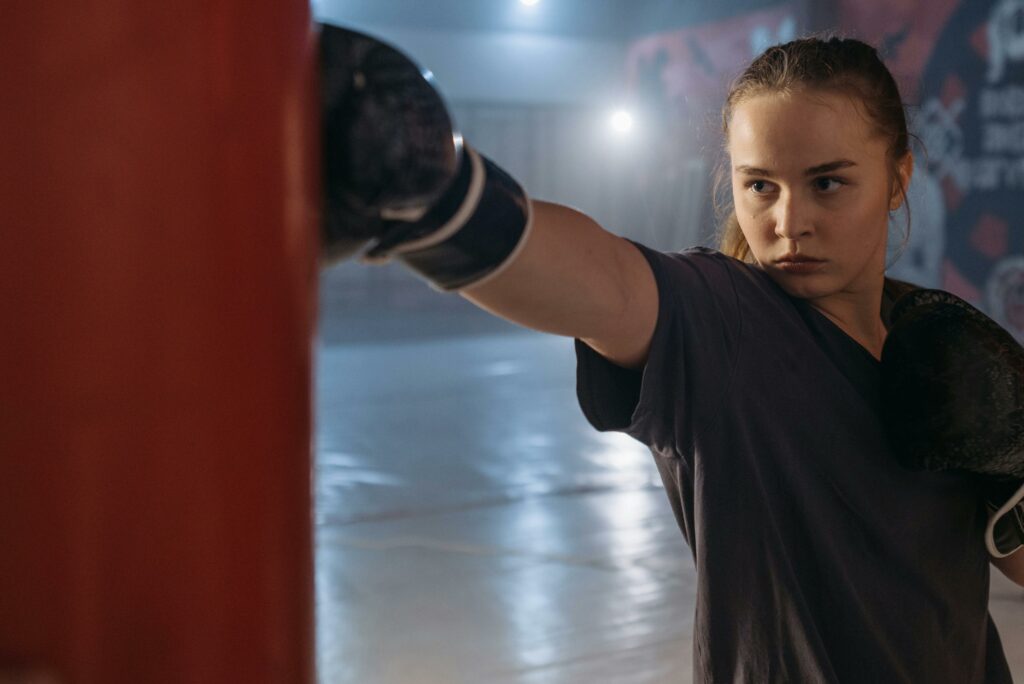 A determined woman boxer in gloves practicing punch on a punching bag in a gym.